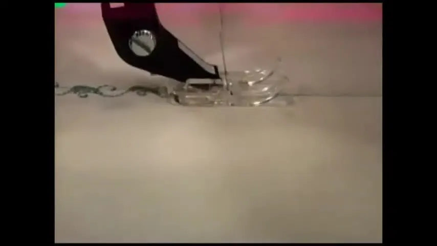 An extreme close-up shows a sewing machine foot stitching a green decorative vine pattern on white fabric.