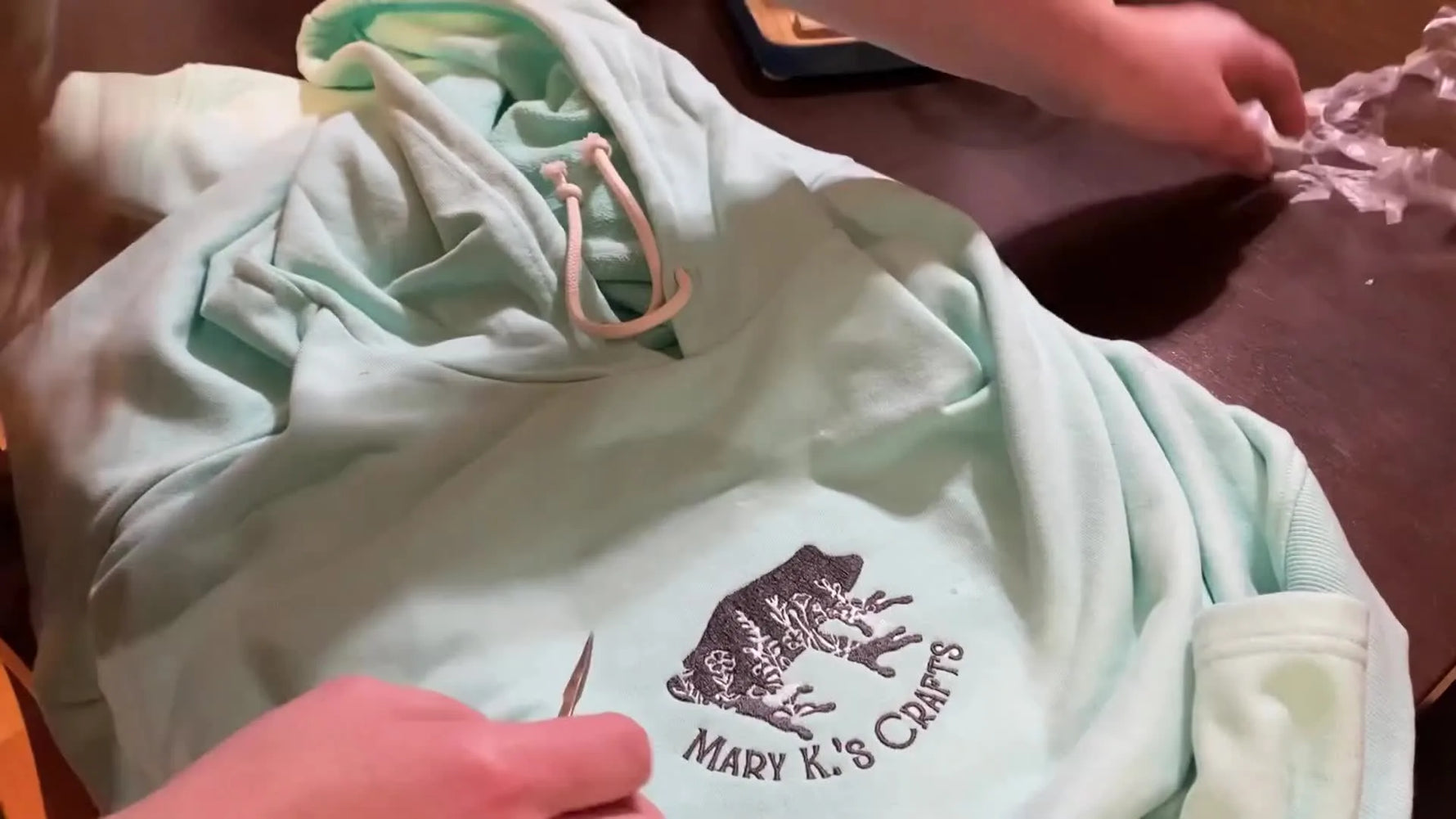 A mint green hoodie laid flat with a finished charcoal logo centered on the chest, showing crisp fill stitches and clean lettering.