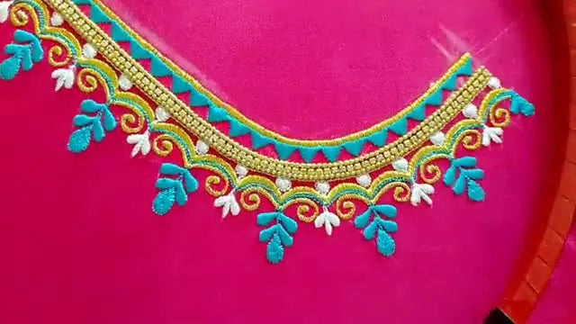 A finished U-shaped neckline embroidery on hot pink silk shows crisp gold borders, teal geometric fills, and delicate floral accents in a balanced, symmetrical layout.