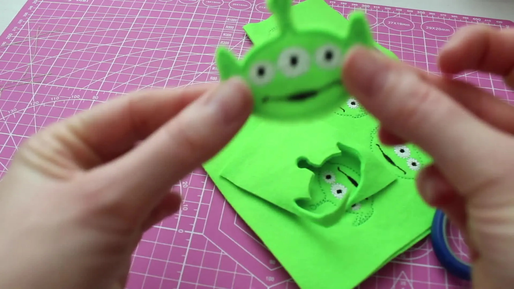 A close-up of the finished Toy Story Alien feltie being held up to the camera, showing crisp stitching and a clean outline edge.