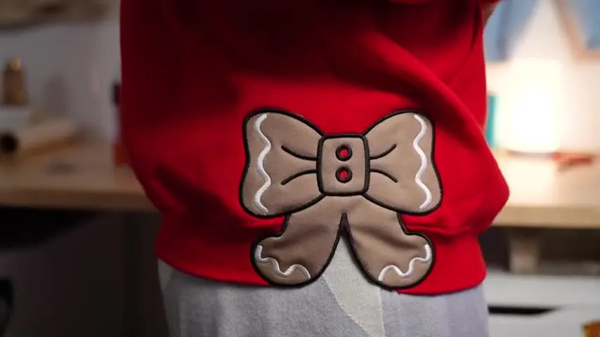A model wears the red hoodie showing the gingerbread bow appliqué stitched cleanly along the side seam.