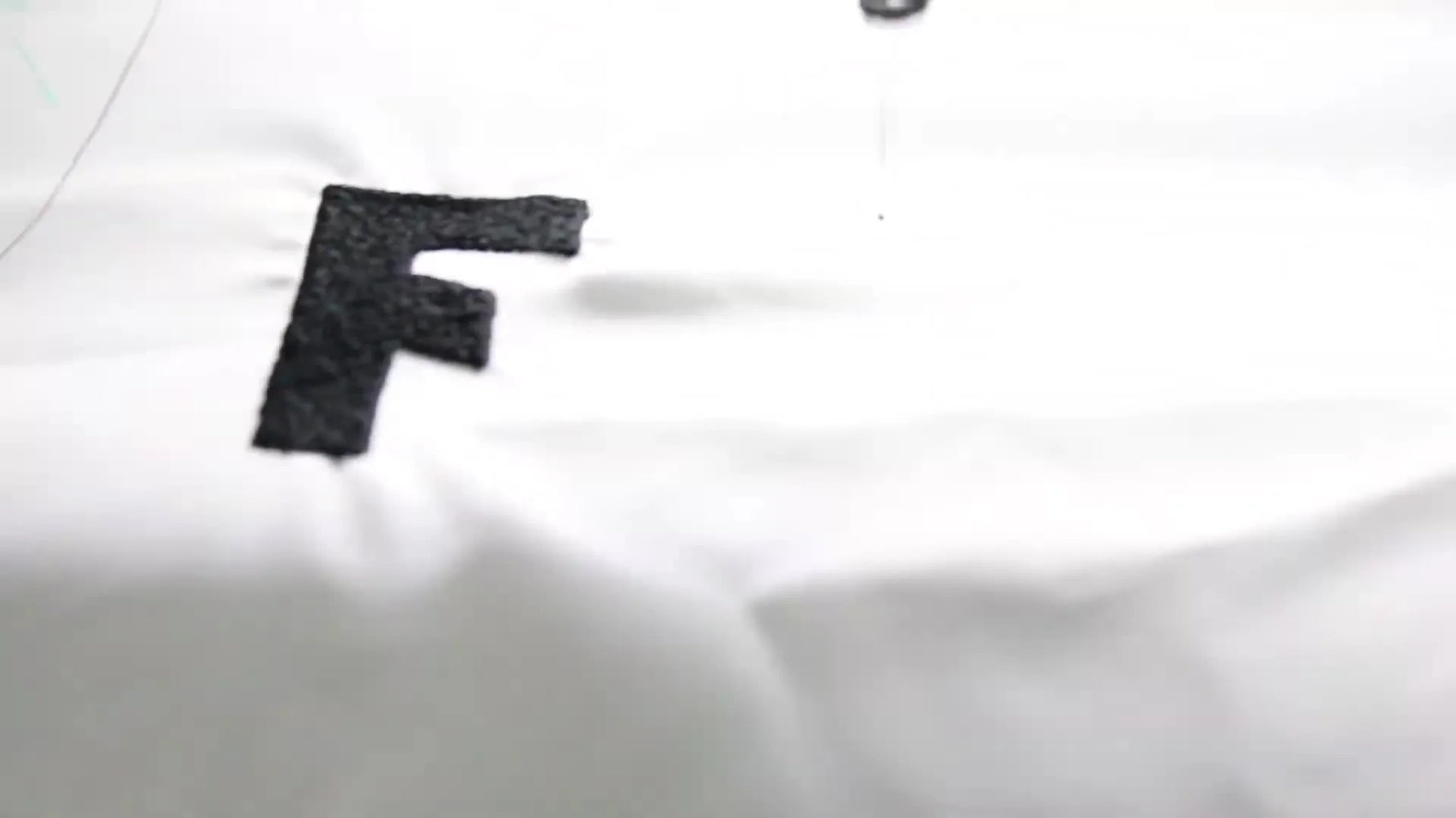 A close-up of a multi-needle embroidery machine stitching a dense black fill on white fabric inside a green tubular hoop.