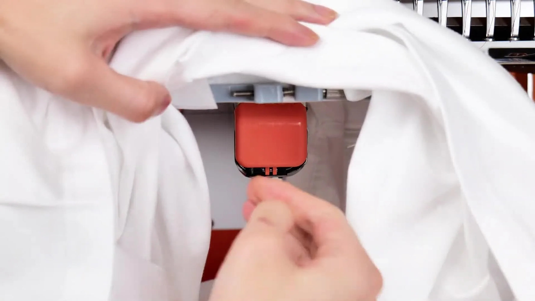 A close-up of the Poolin machine actively stitching a red heart design onto a finished white T-shirt.