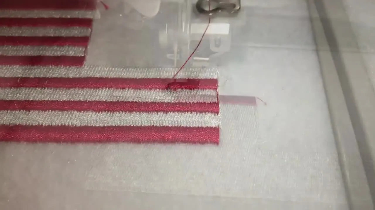 A 5x7 hoop shows the reverse American flag patch mid-process with crisp red stripes stitched on white felt.
