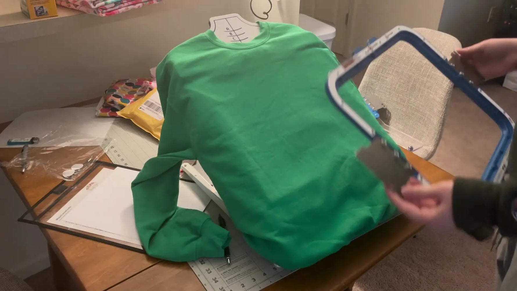 The top magnetic hoop frame is aligned over a centered sweatshirt on the Mighty Hoop Station just before the magnets snap shut.