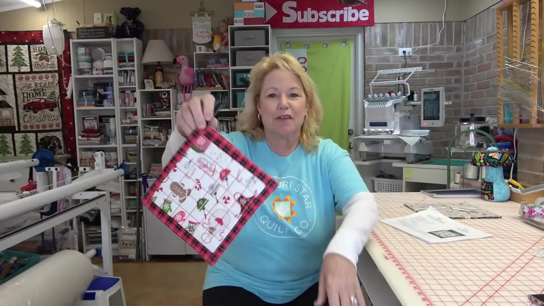 A finished red-and-white Christmas-themed in-the-hoop pot holder is held up to show the clean quilting, borders, and hanging loop.