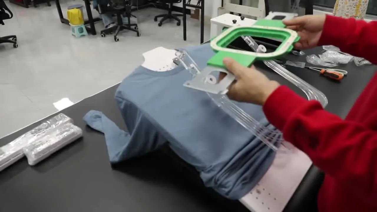 Hands place the top magnetic hoop onto a T-shirt on the HoopTalent station, capturing the moment the fabric is clamped flat and ready to stitch.