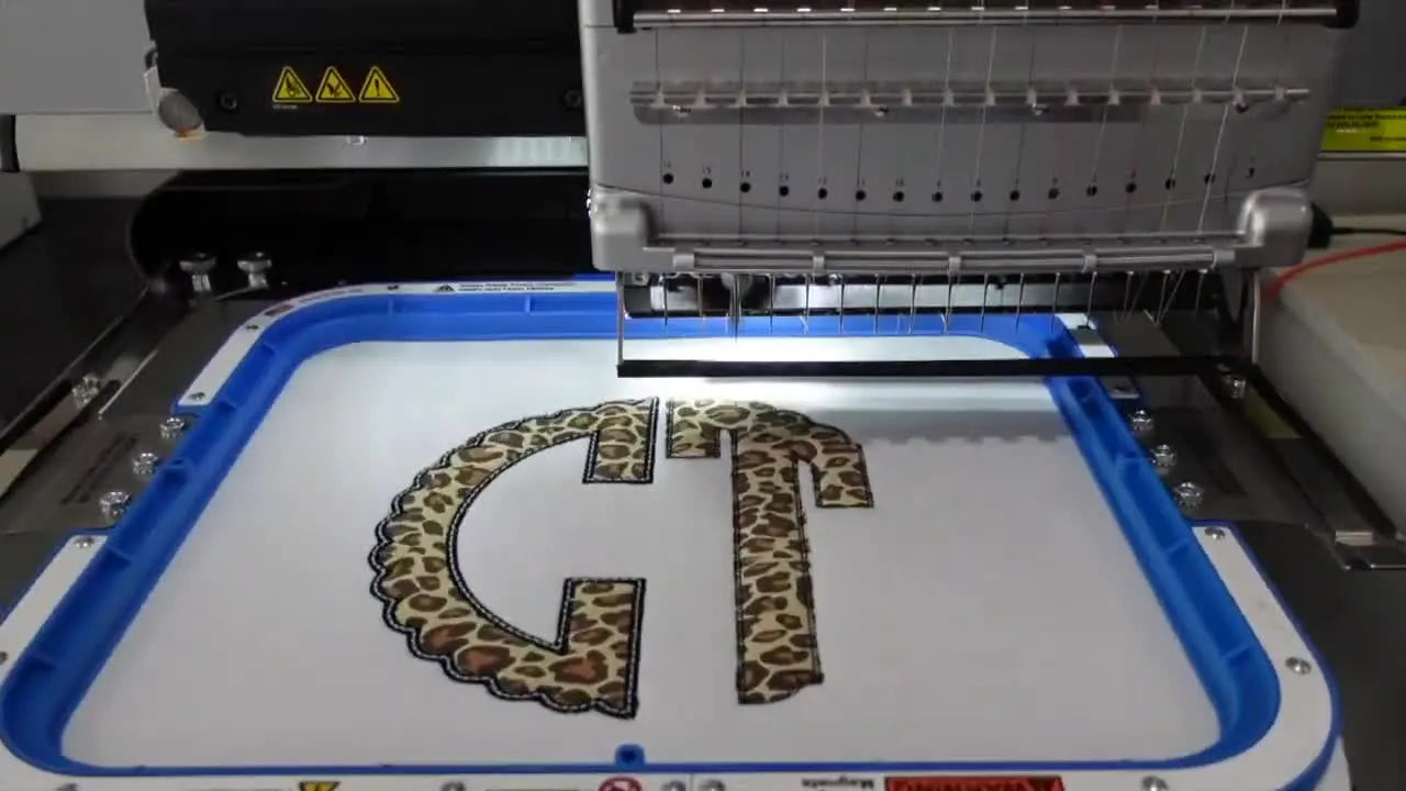 A close-up of the Melco machine stitching a dense satin border that cleanly seals the edge of a leopard flocked HTV appliqué.