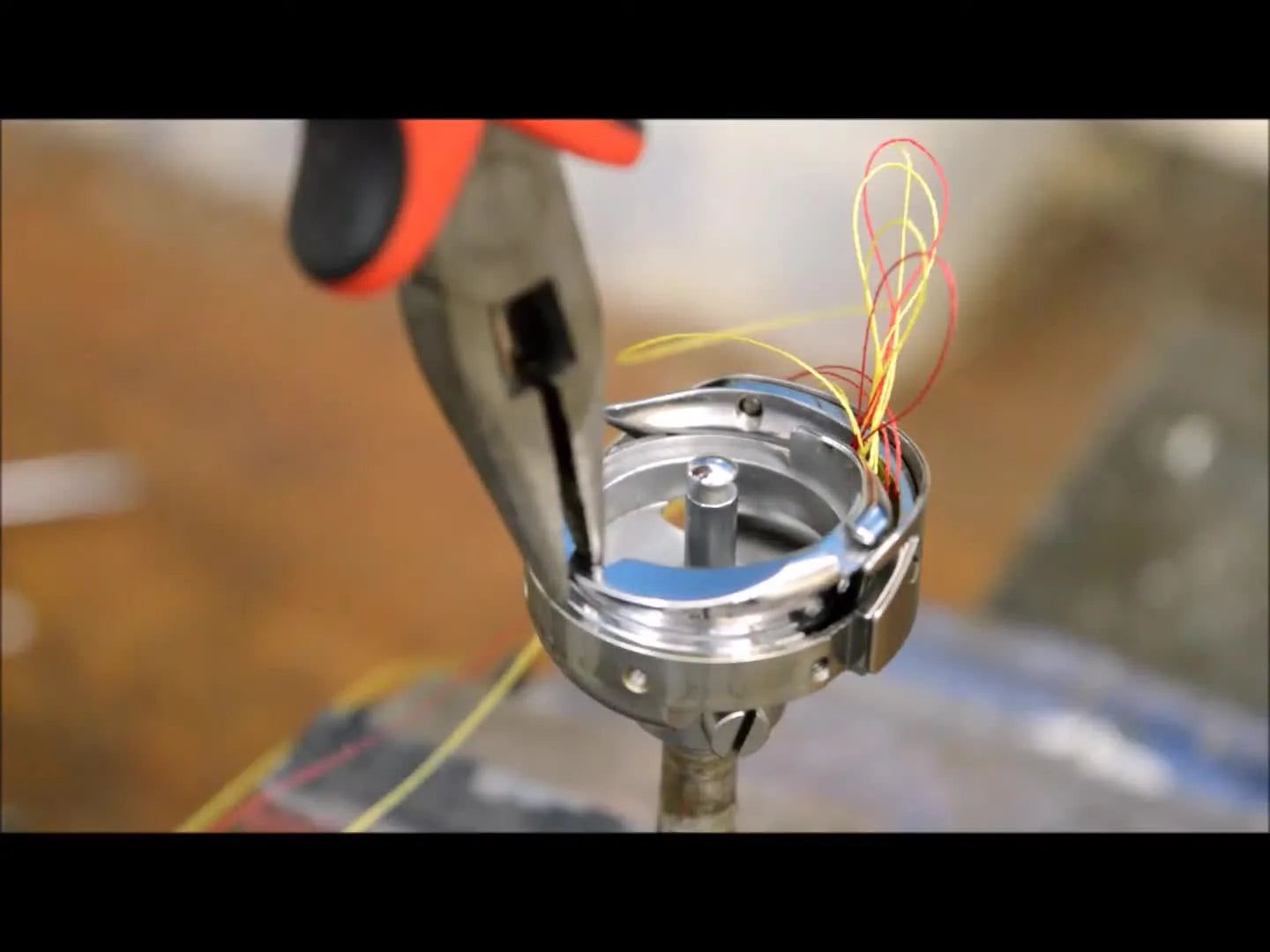 Pliers grip the inner rotary hook basket to break a severe thread jam free inside the hook race.