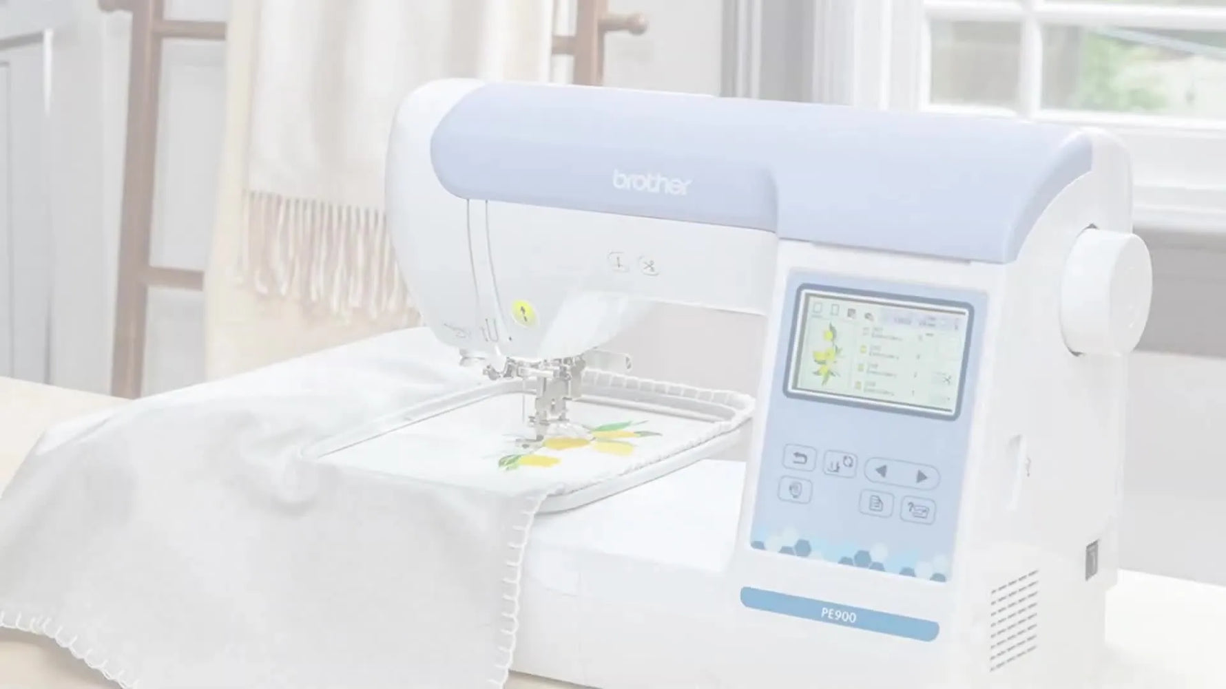 A Brother PE900 stitches a lemon design on grey fabric while thread spools sit behind it, showing an active, real-world embroidery setup.