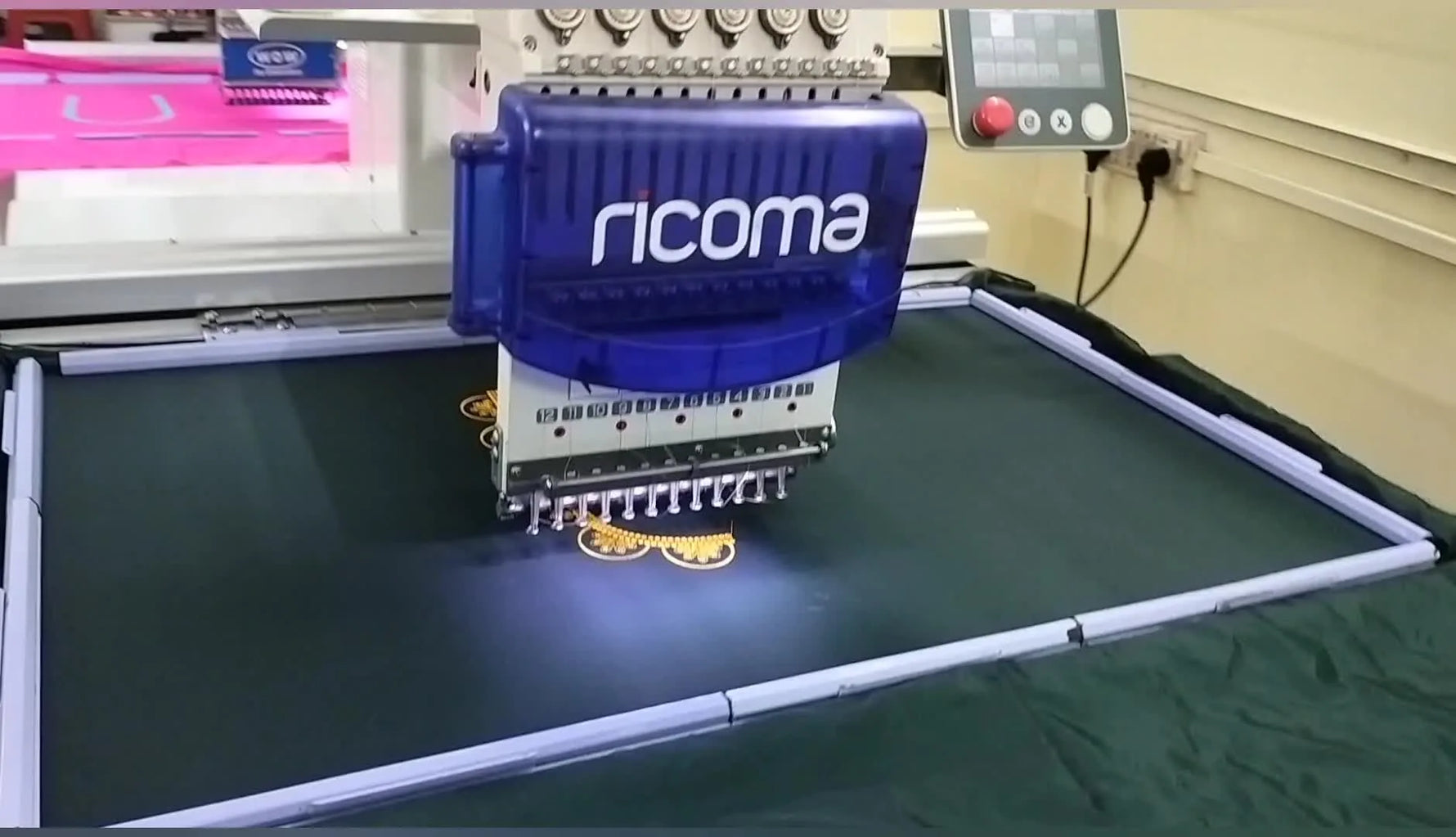 A multi-needle embroidery machine stitches a gold design while a large rectangular magnetic sash frame clamps black fabric flat for stable, fast production.