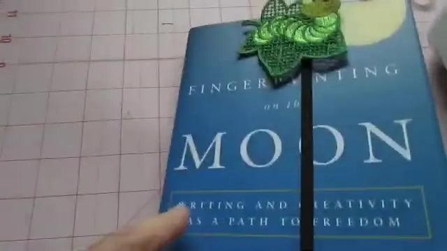 A finished elastic book band bookmark wrapped around a hardcover book, showing the FSL bookworm centered over the elastic seam.