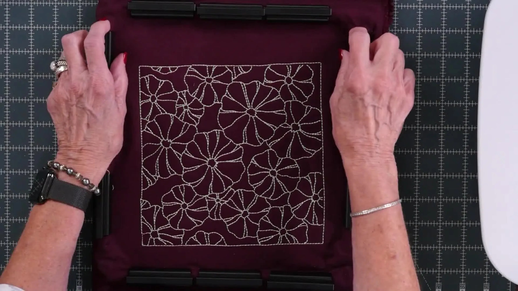 An overhead view shows a magnetic clamp hoop holding a thick quilt sandwich securely for embroidery placement and stitching.