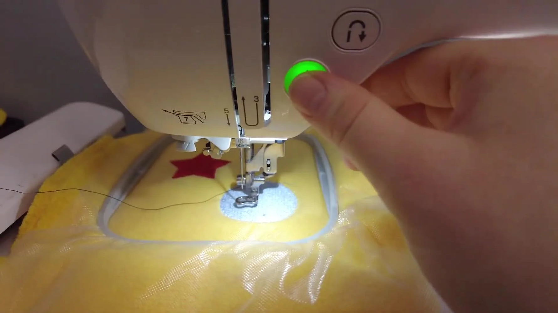 A close-up of a finger pressing the green Start/Stop button to begin stitching on a Brother embroidery machine.