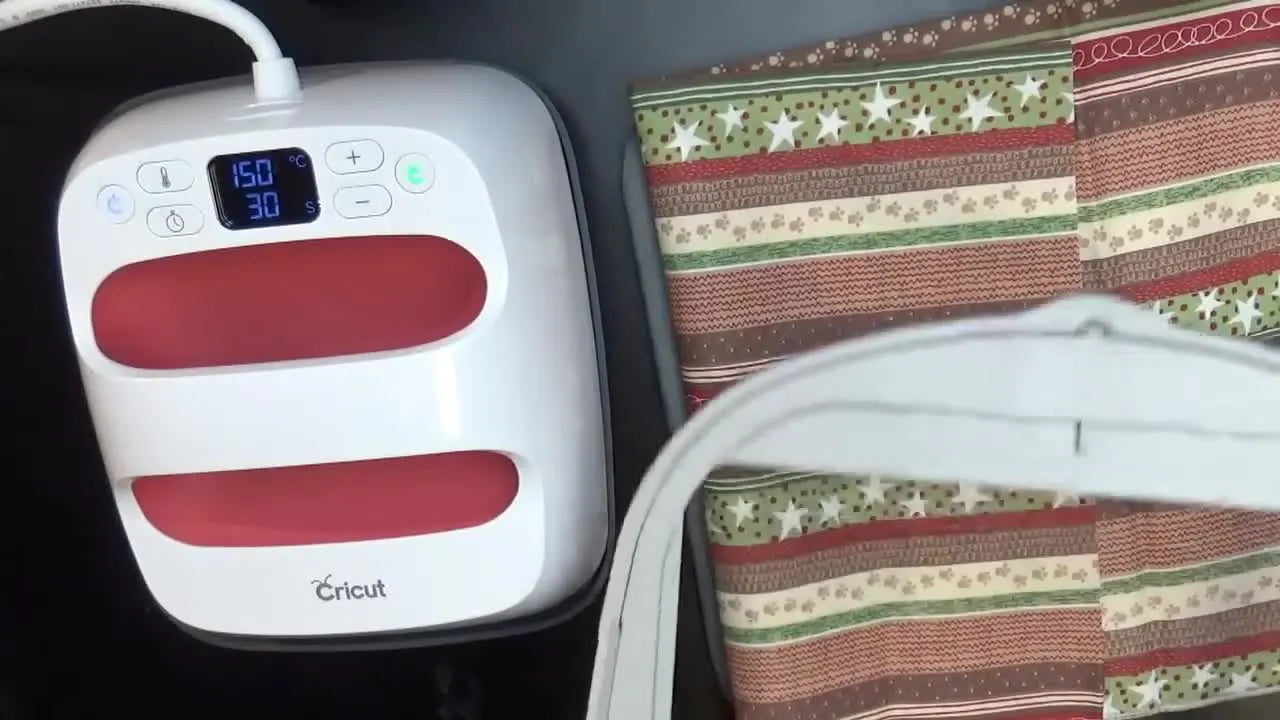 A Cricut EasyPress Mini is being used to press fabric directly inside a square embroidery hoop without unhooping.
