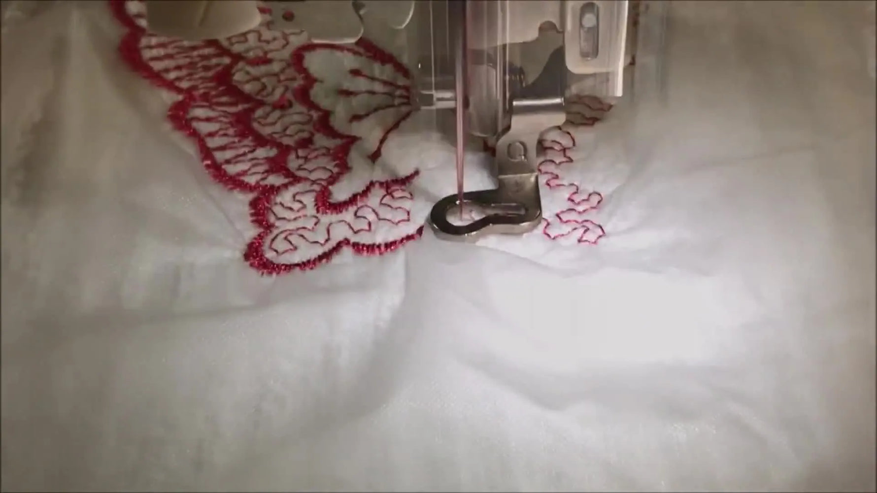 A close-up action shot of a Brother SE425 stitching a red butterfly through clear Sol-U-Film on a floated white towel.