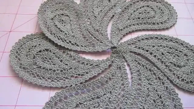 Seven washed and dried freestanding lace paisleys are arranged into a precise pinwheel circle on a gridded cutting mat, ready for assembly.