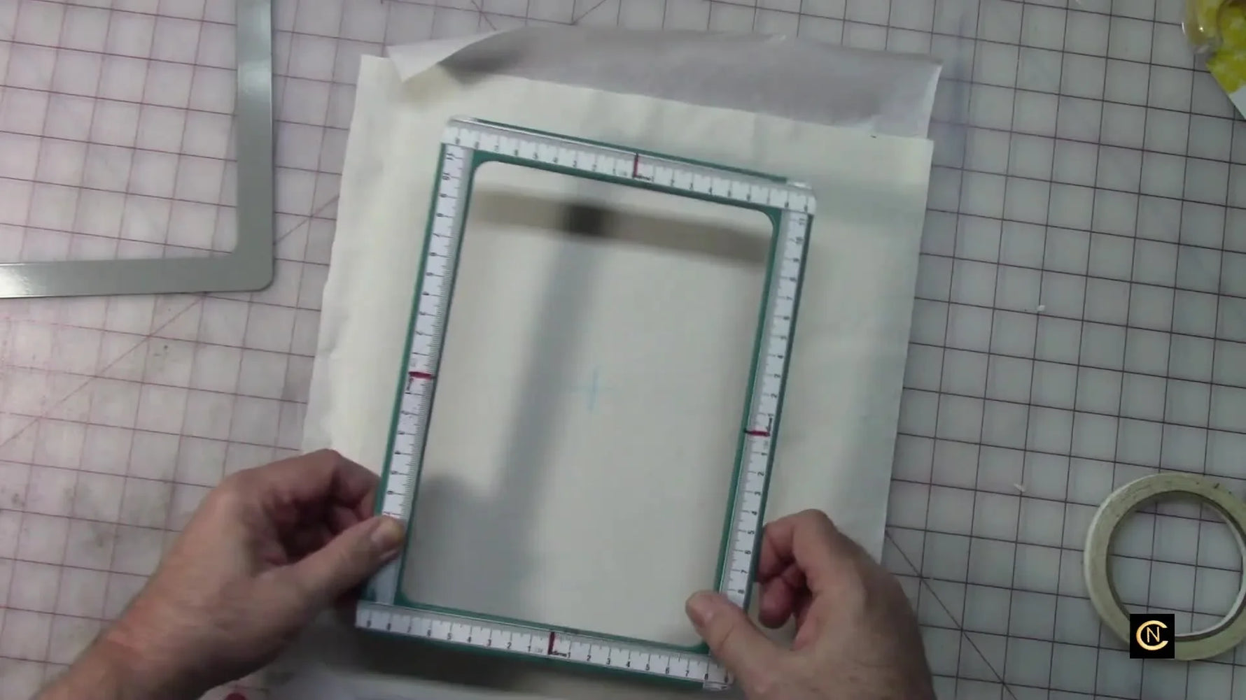 A taped magnetic hoop top frame is carefully aligned over chalk crosshair marks on fabric for precise embroidery placement.