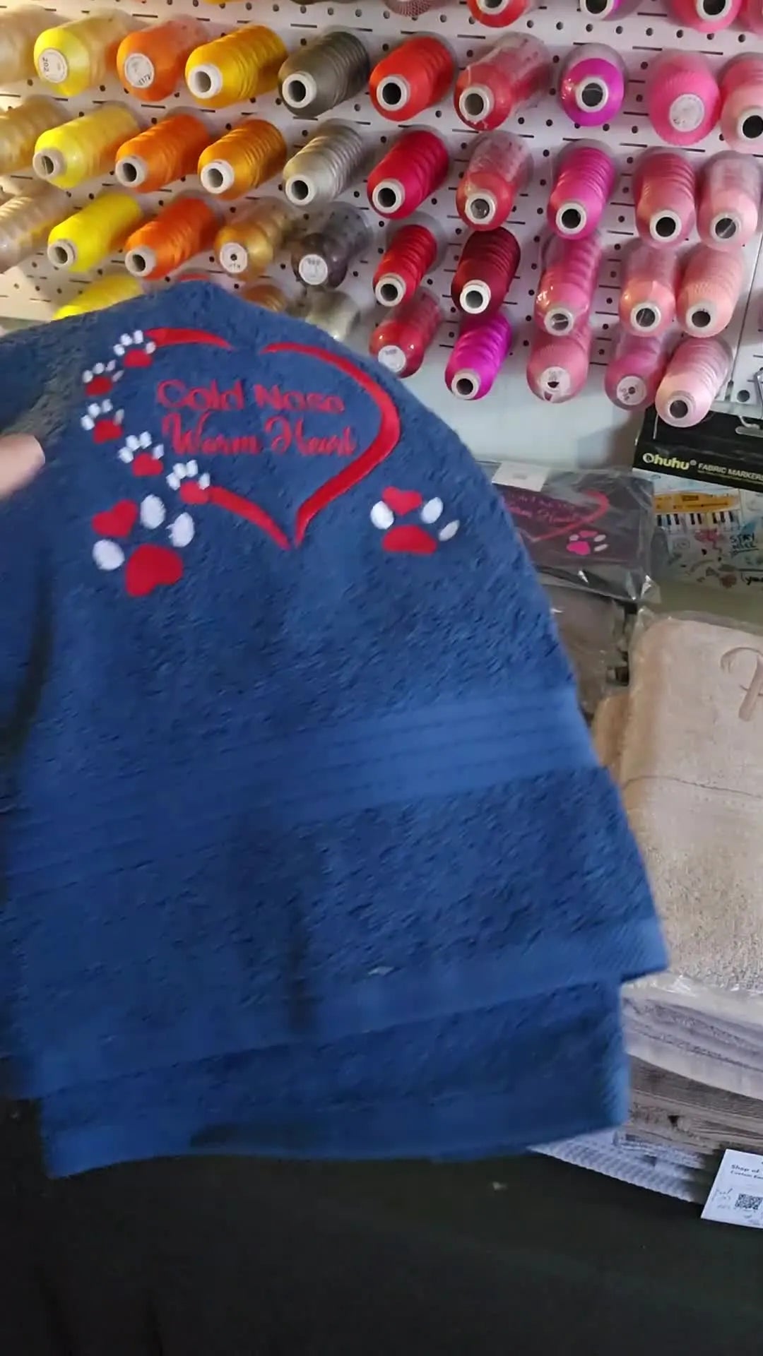 A close-up of a blue plush towel embroidered with a paw-print and heart design, showing crisp lettering and clean coverage on textured fabric.