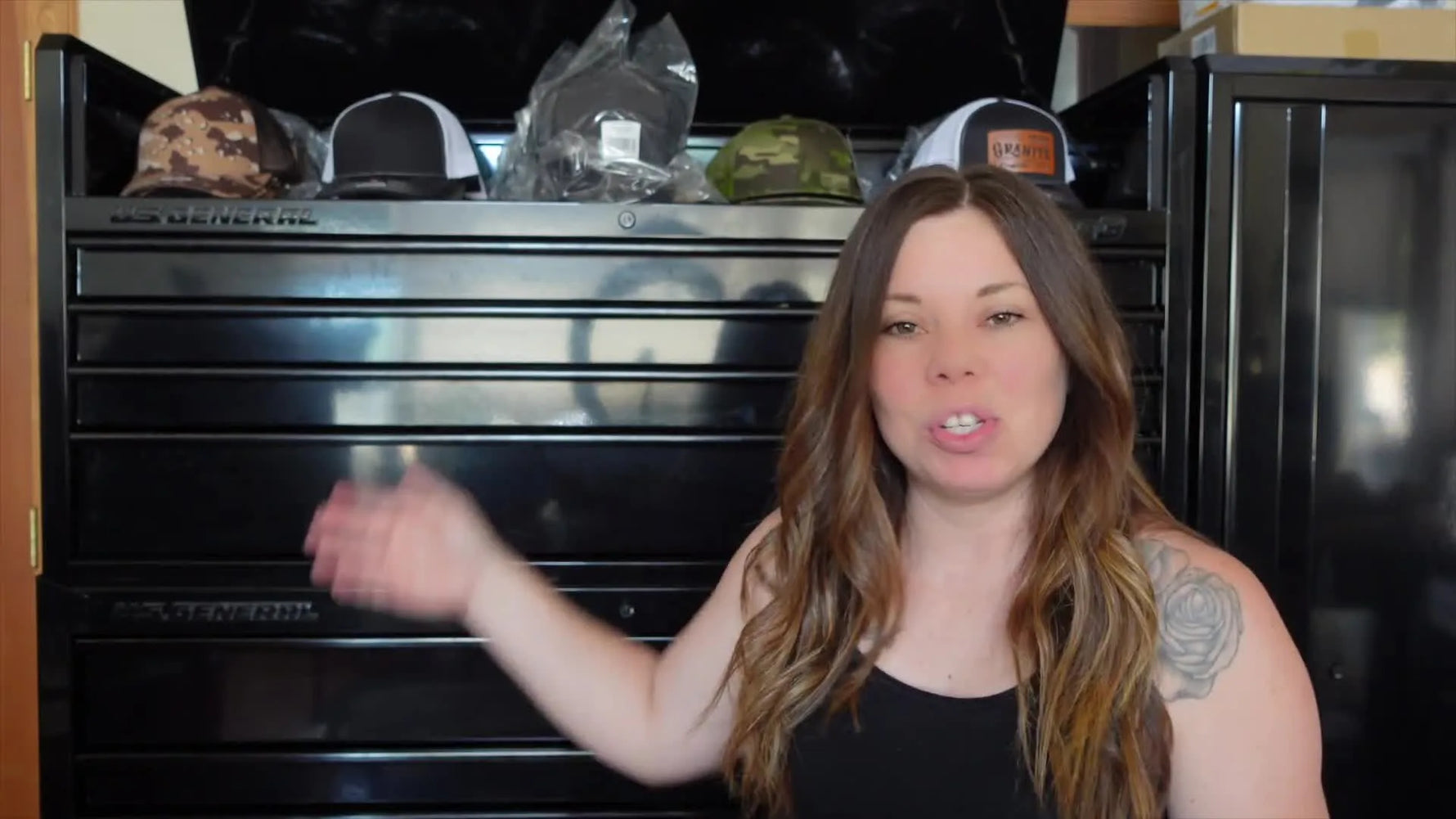 Woman standing in front of a large black toolbox, gesturing towards it.