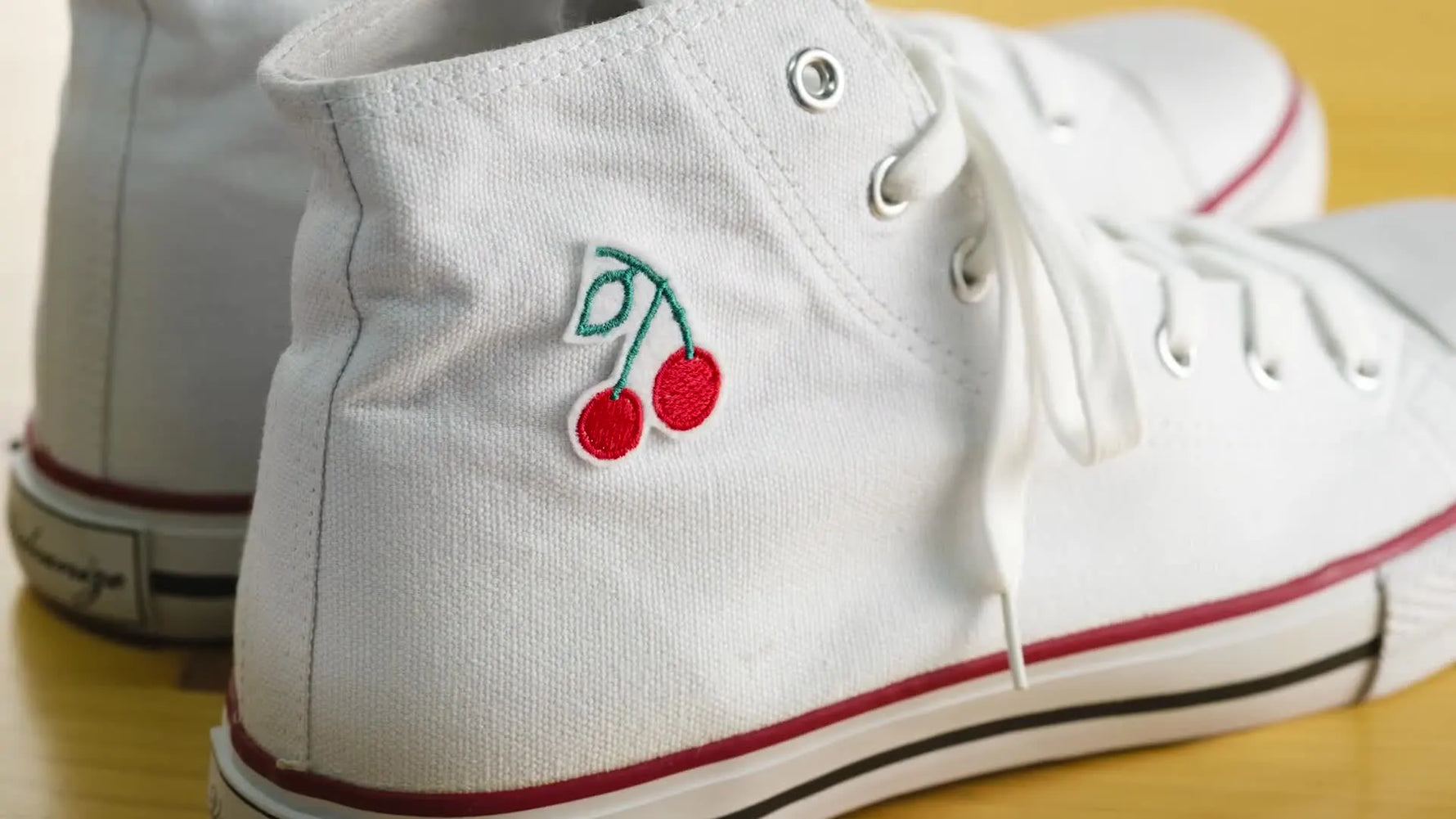 A finished cherry embroidery design stitched on the side of a white high-top sneaker.