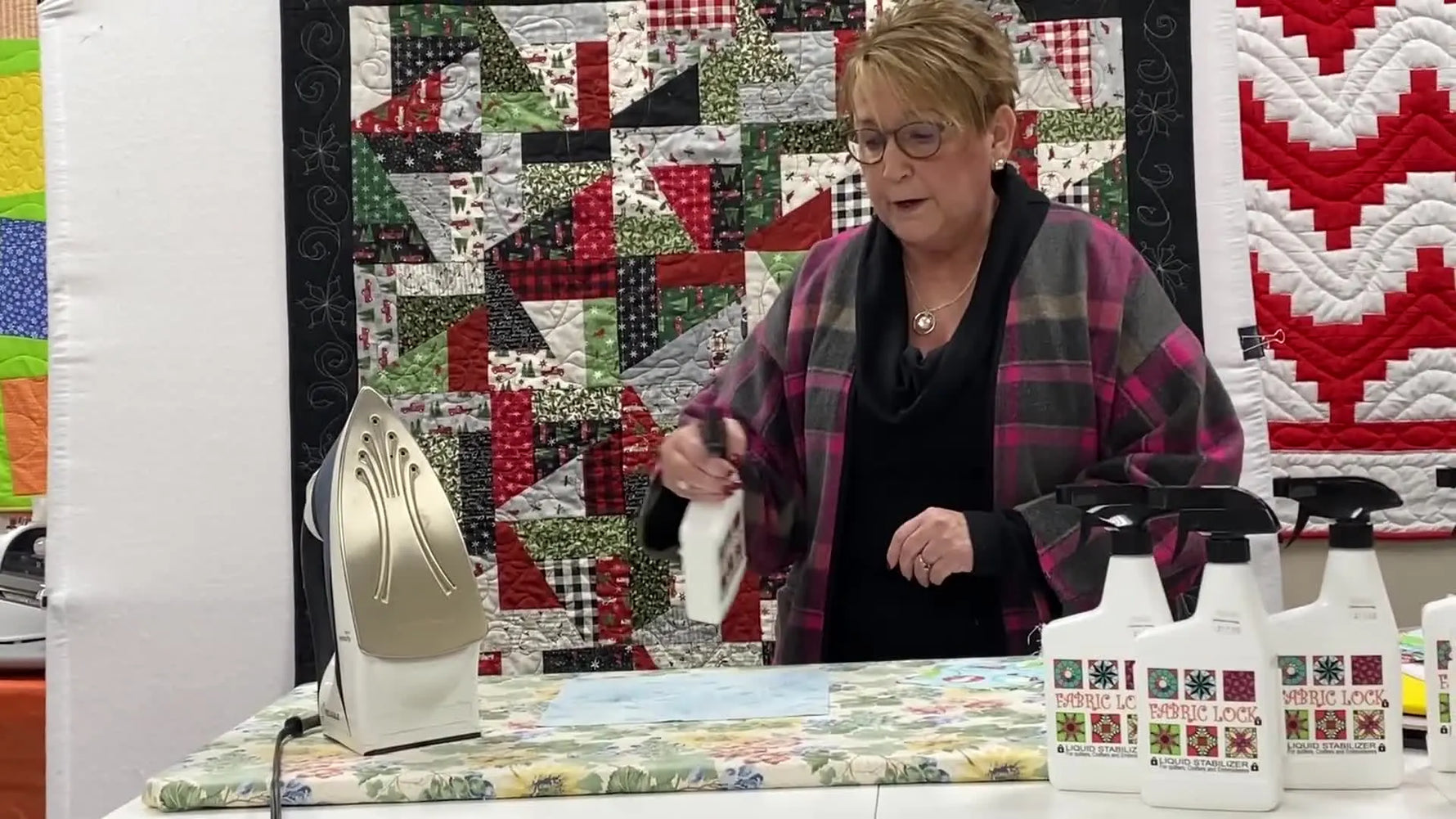 A close action shot shows Fabric Lock being sprayed onto fabric at a 45-degree angle to stiffen it before hooping or piecing.