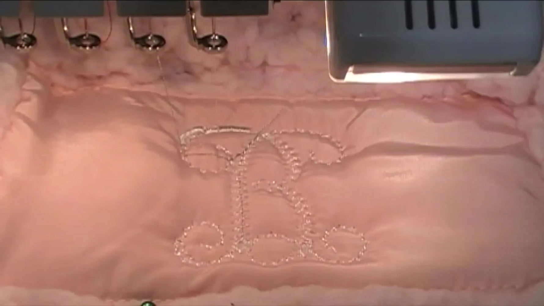 A close-up of a finished white monogram stitched cleanly on pink Sherpa while still mounted on the machine.