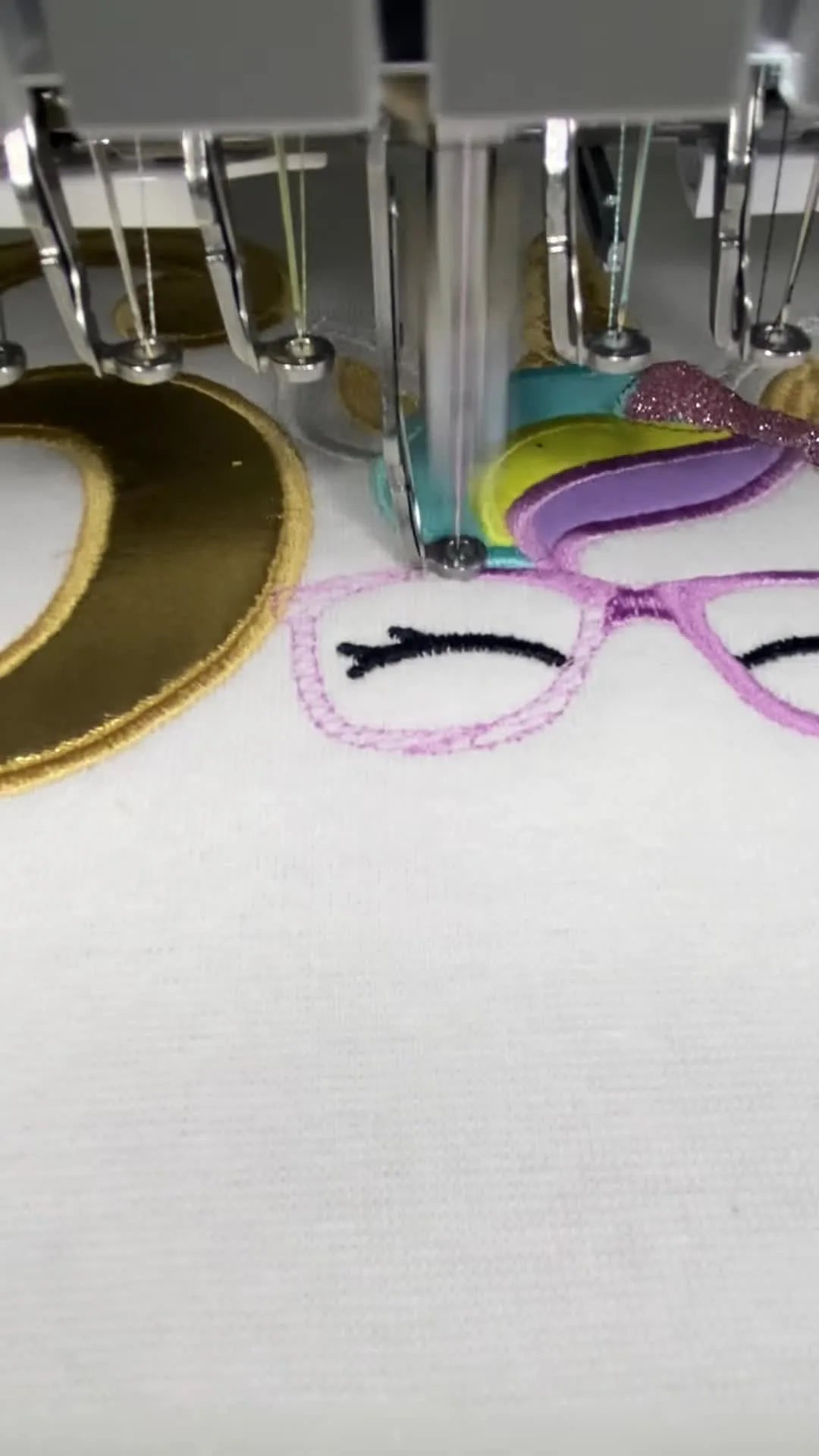 A wide view of a white magnetic hoop holding a nearly finished unicorn-and-gold-appliqué birthday design, with safety warning labels visible on the frame.