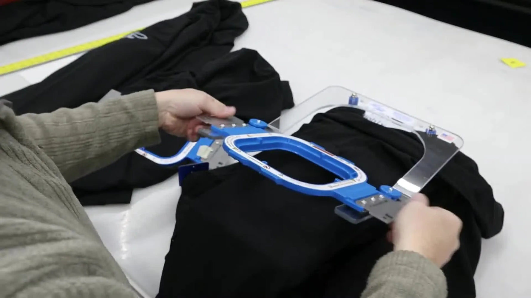 Hands snap a magnetic hoop onto a jacket sleeve on a hooping station, capturing the exact moment the fabric is clamped flat and ready for production.