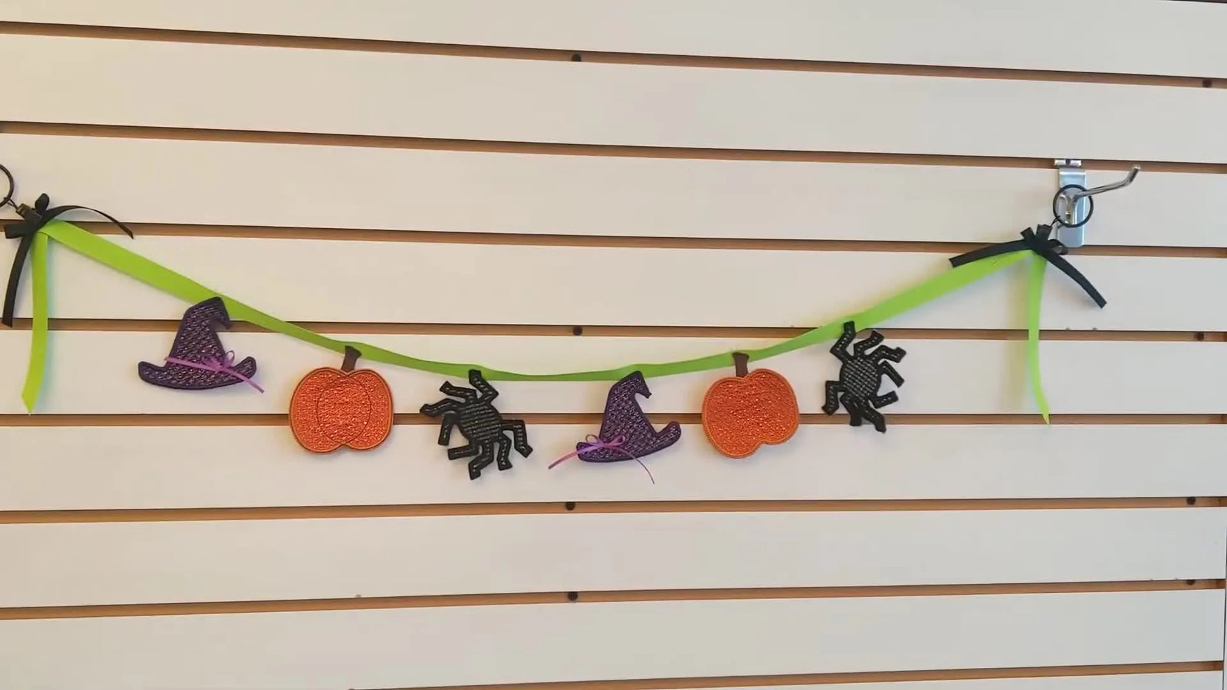 A finished Halloween garland with freestanding lace spiders, pumpkins, and witch hats hanging on a wall.