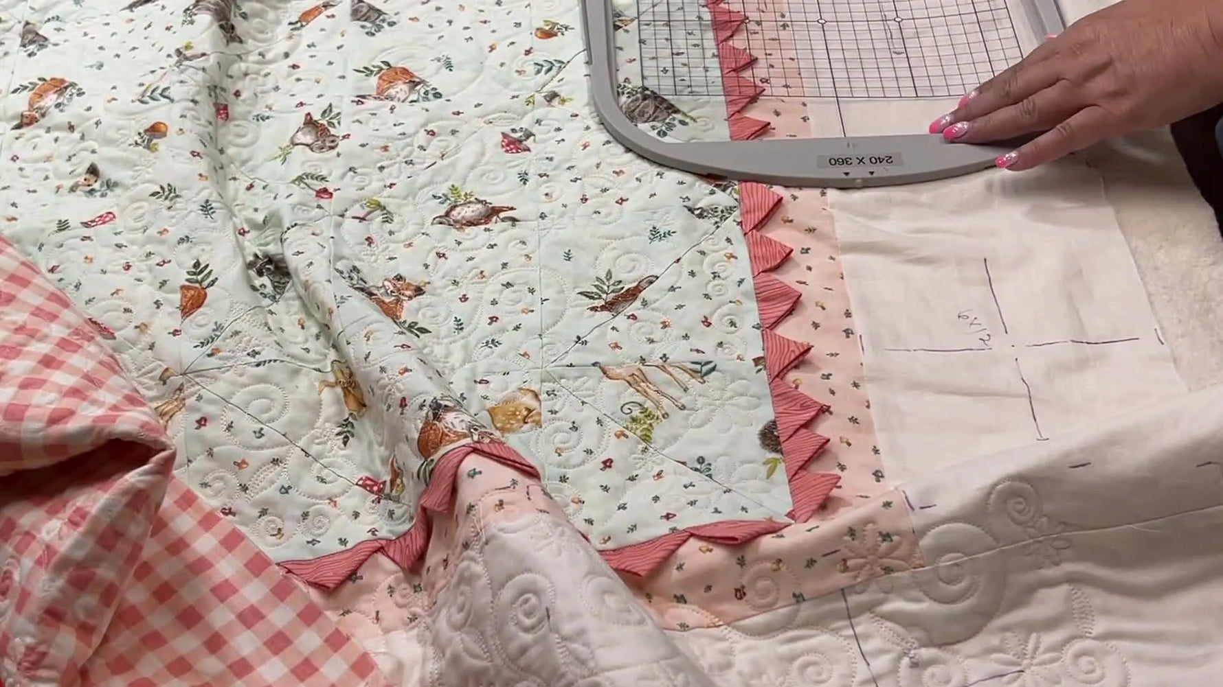 Hands use a plastic grid template inside a 240 x 360 hoop to align marked crosshairs on a quilt border before stitching.