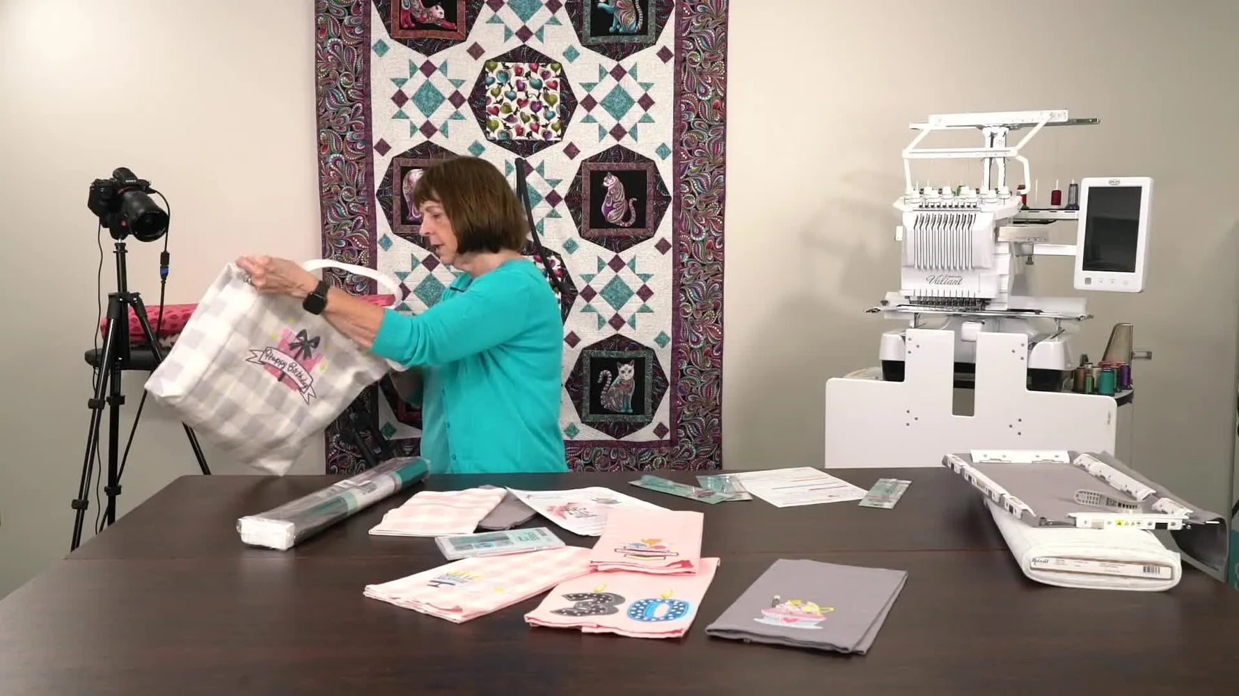 A finished grey-and-white buffalo check tote bag is held up to show a bold “Happy Birthday” embroidery design on the front.