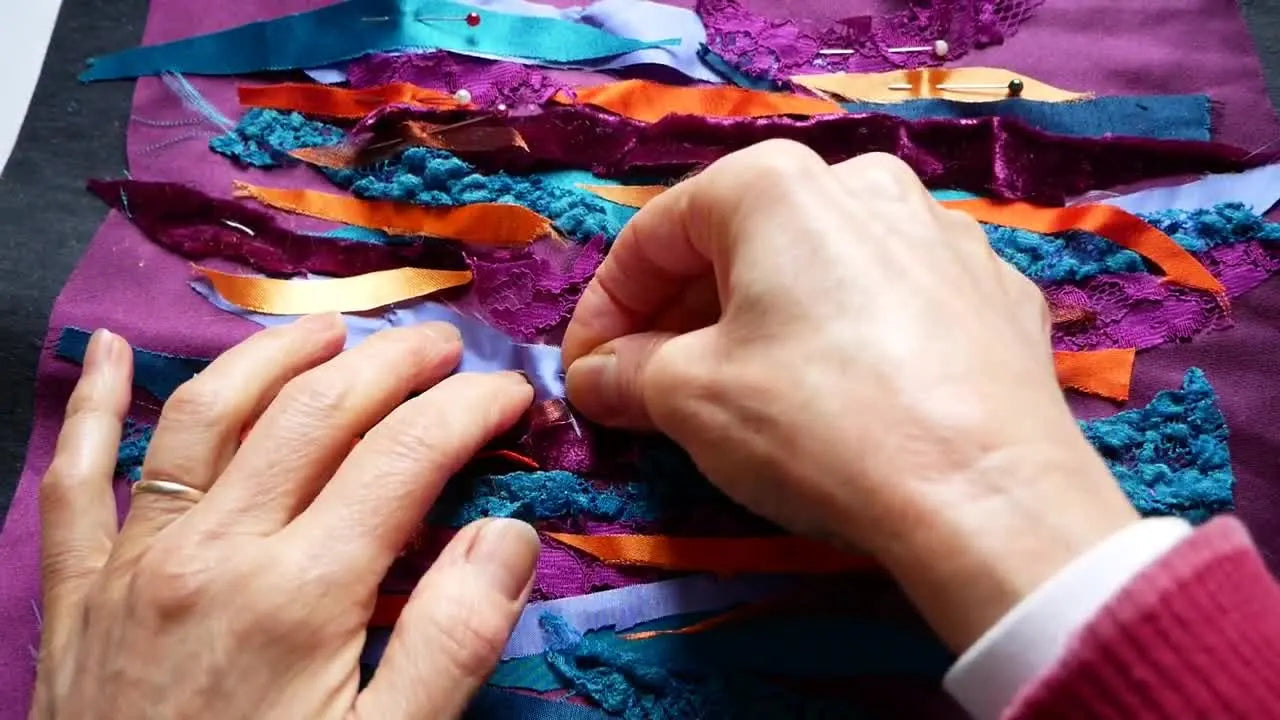 Close-up of hands pinning down various colored fabric strips onto a purple background.