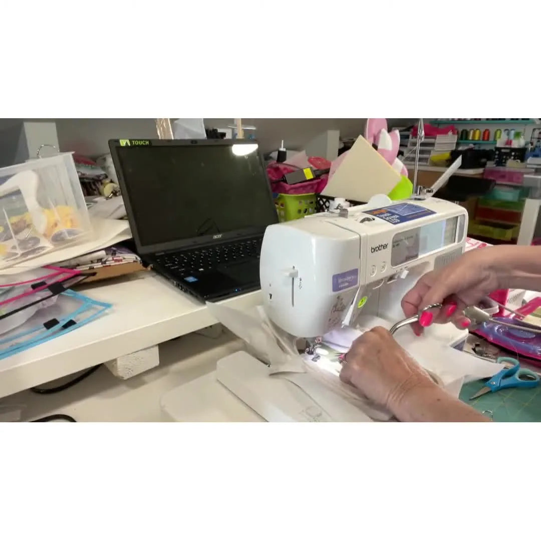 Close-up of trimming appliqué fabric with curved scissors while the hooped onesie remains attached to the Brother SE400 for perfect registration.