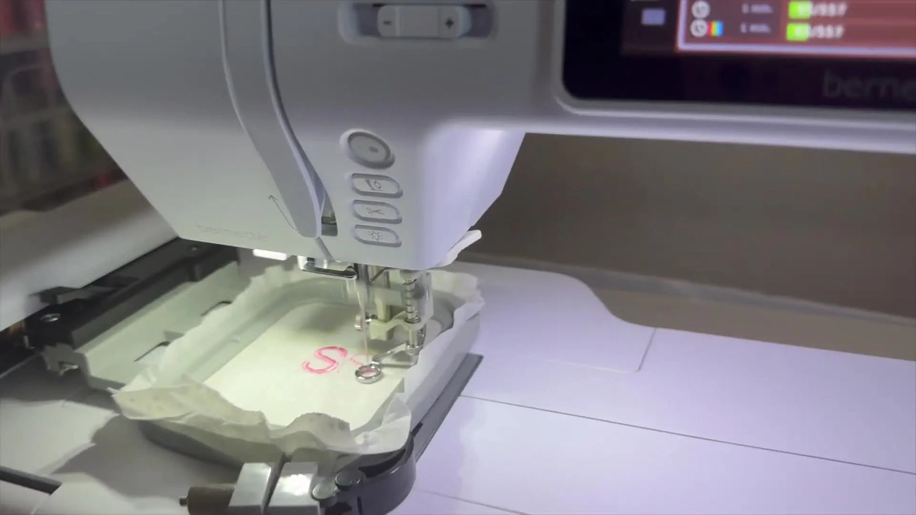 Close-up action shot of the Bernette Deco B70 needle stitching a pink satin letter “S” on hooped white fabric.