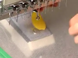 An extreme close-up shows the embroidery machine forming a dense satin stitch border around a yellow applique petal edge.