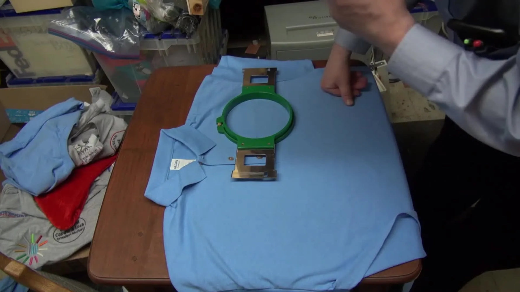 Hands hold a green magnetic hoop above a polo shirt, ready to snap down for fast, accurate hooping.