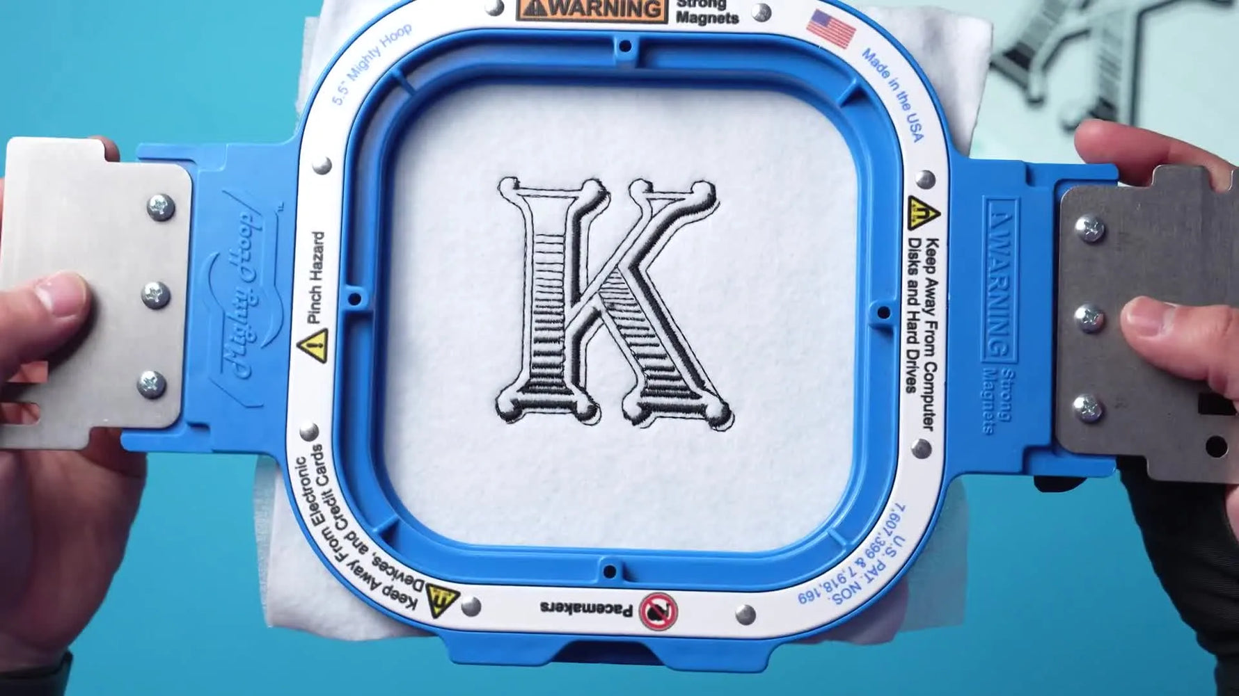 A close-up of a blue magnetic hoop holding the finished embroidered vintage-style letter “K”.
