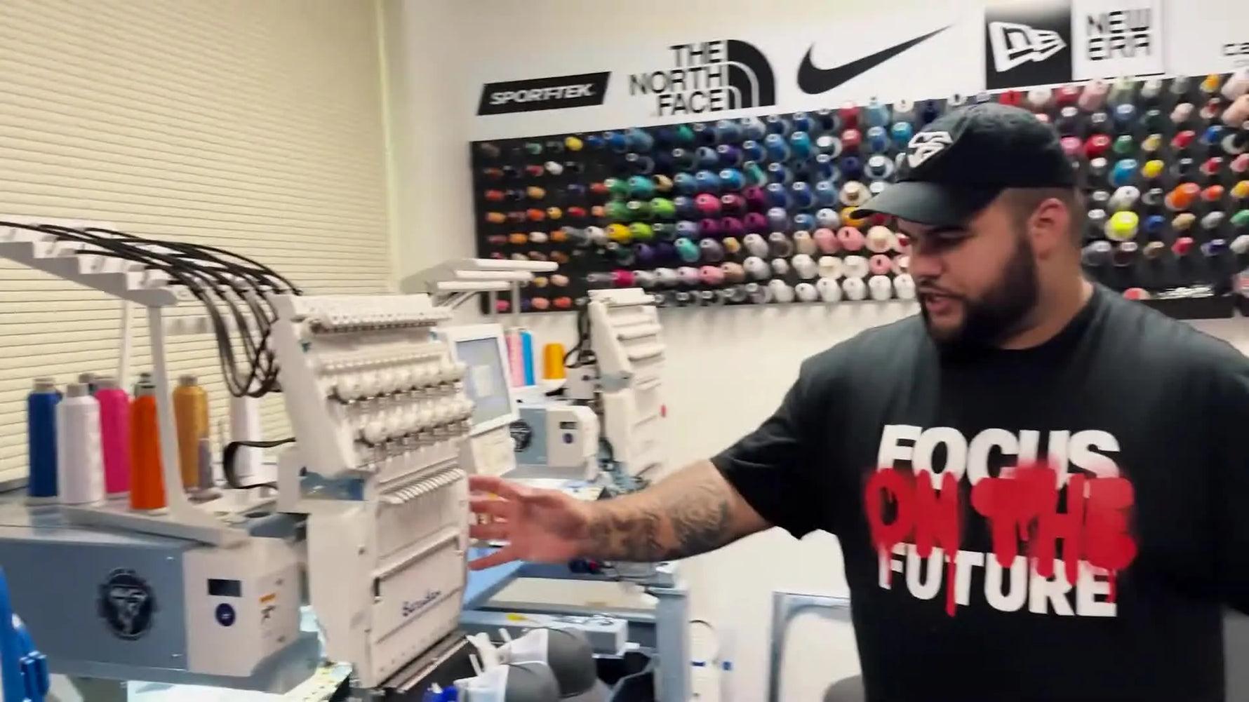 The shop owner stands beside a Barudan Pro 3 in the embroidery production area, highlighting a compact commercial setup built for daily output.