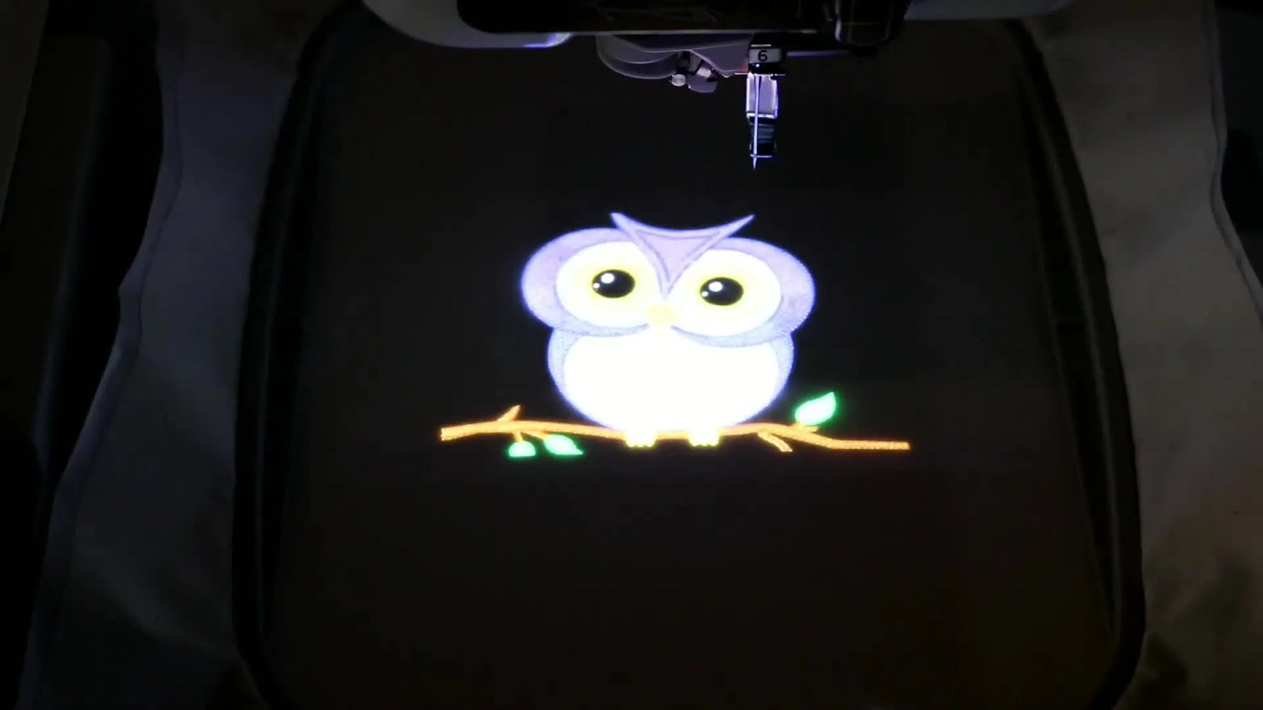 A bright owl embroidery design is projected onto dark fabric inside a hoop, showing the Baby Lock Solaris IQ Visionary placement feature.
