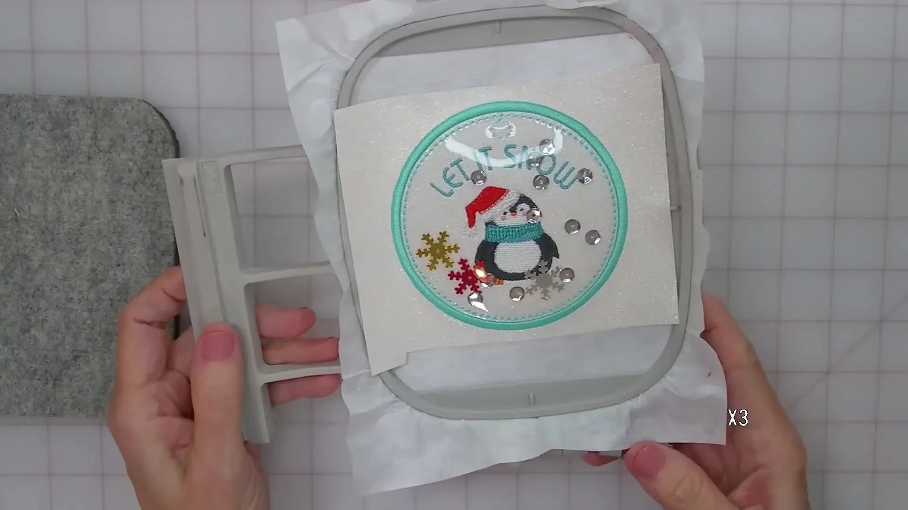 A fully stitched confetti shaker bag tag in the hoop, showing the penguin design and loose sequins moving inside the clear vinyl window.