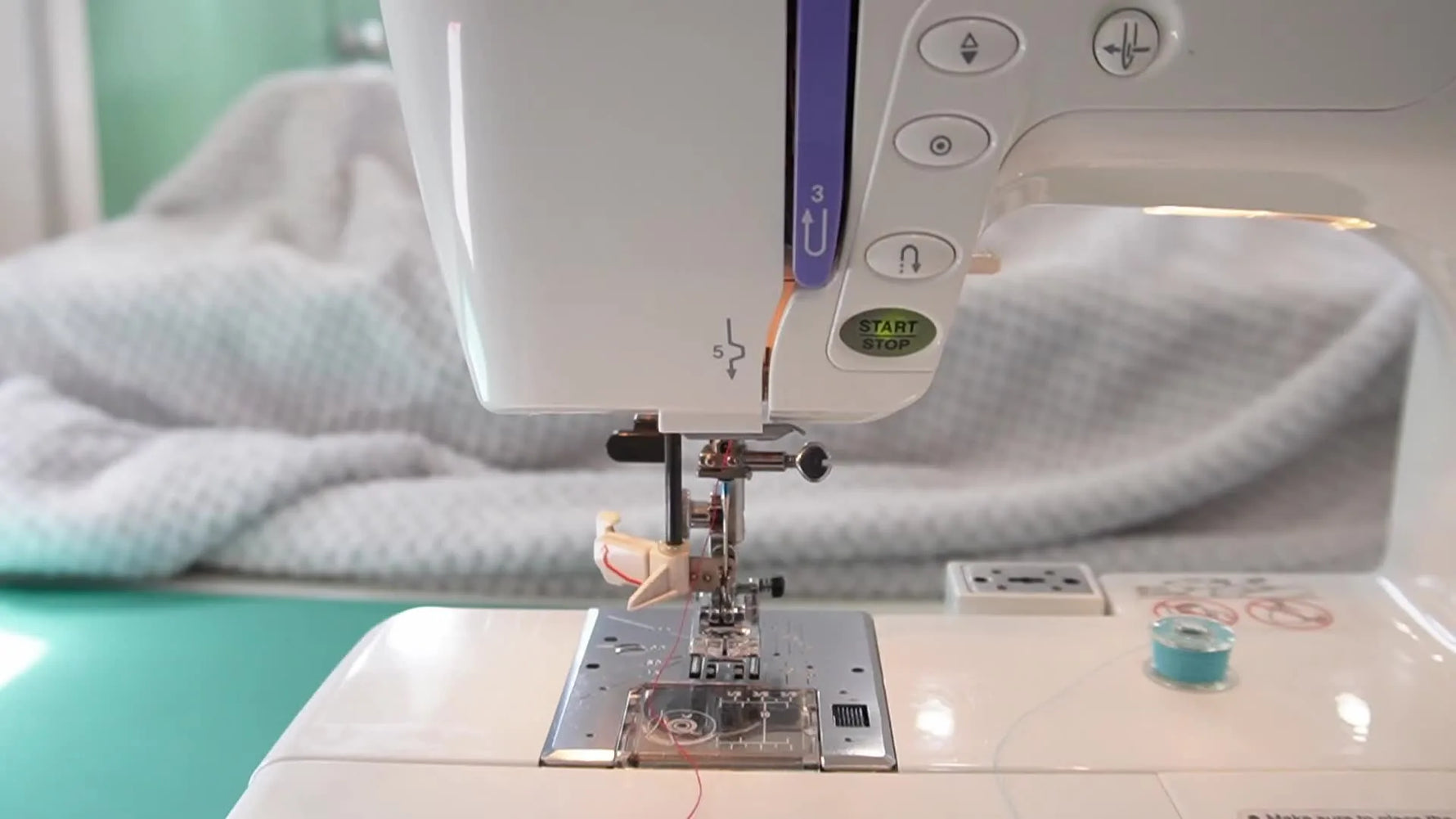 A close-up of the Janome MC10000 automatic needle threader lowered around the needle, showing the exact moment the mechanism forms a thread loop.