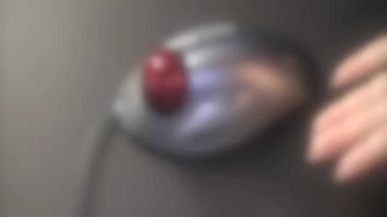 A close-up of the Logitech Trackman Marble mouse showing its distinctive red trackball on a dark work surface.