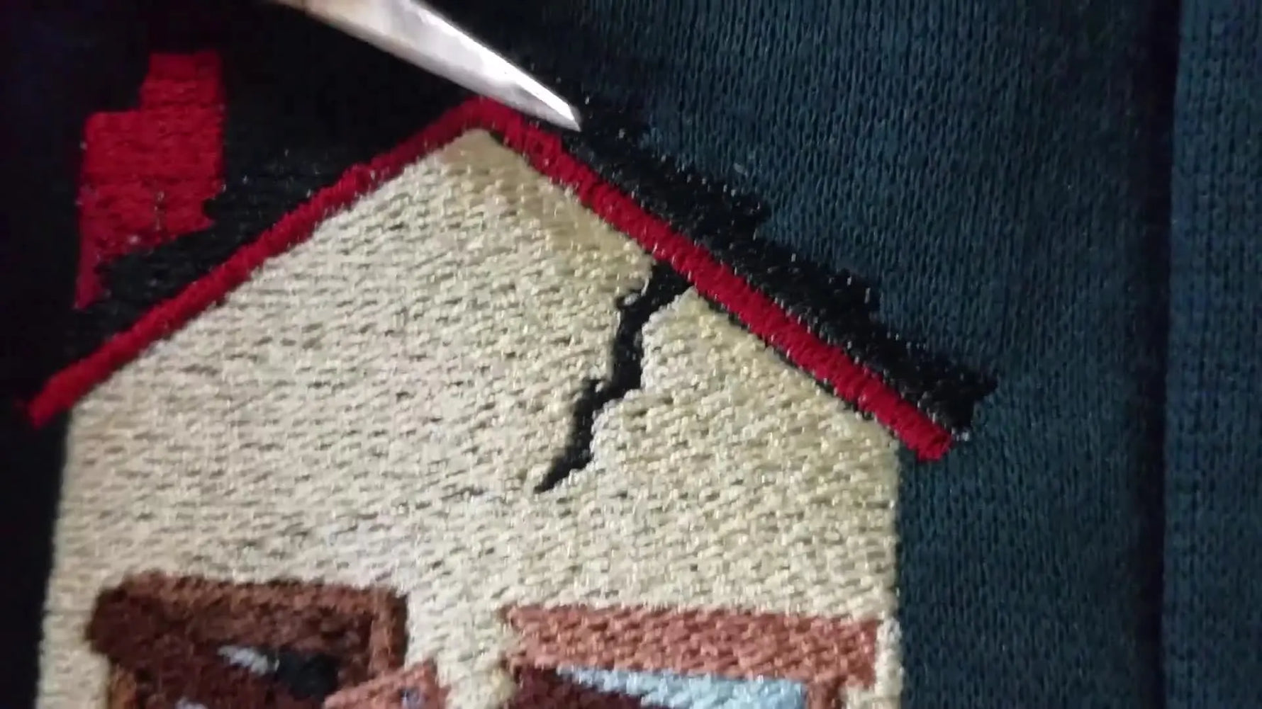 A macro close-up shows a metal pointer highlighting tiny white bobbin specks popping through a black satin stitch border on an embroidered garment.