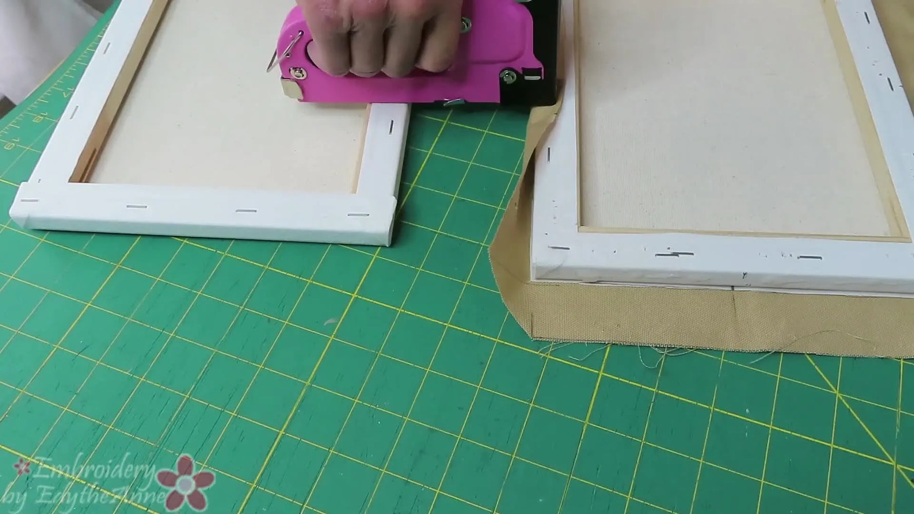 A close-up shows a pink staple gun pressing straight down on the canvas frame while a second spare frame supports the stapler for perfectly aligned staples.