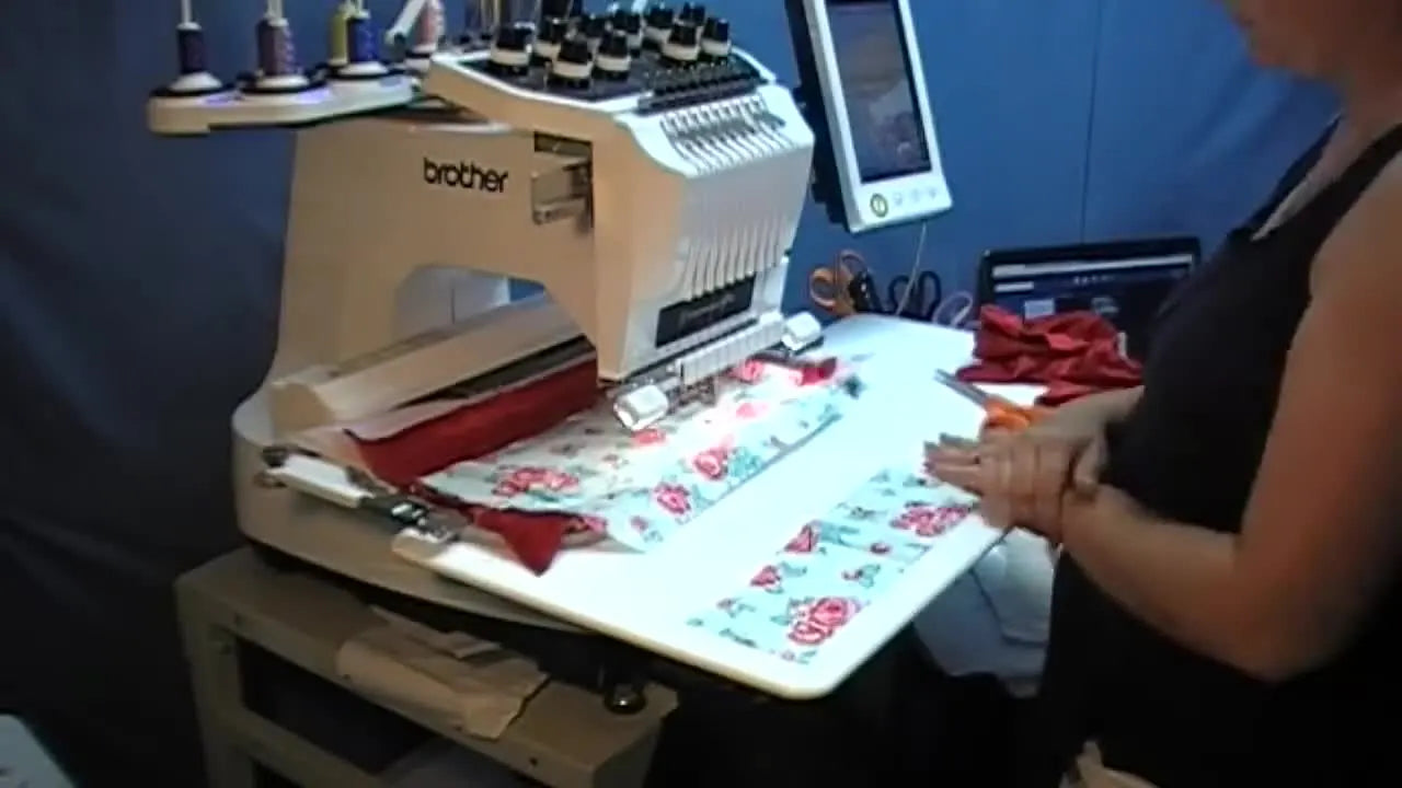 A high-angle close-up shows floral cotton being stitched onto a red minky base inside a 360×200 mm hoop during the ITH applique stage.