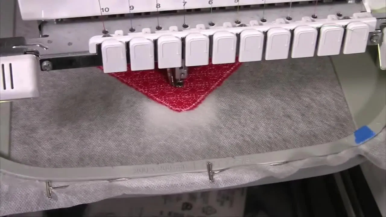 A close-up of the machine stitching the concentric heart design on red felt inside the hoop.
