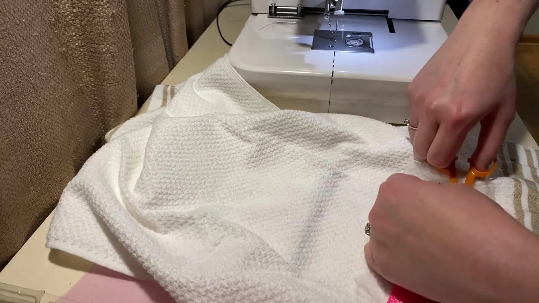 Close-up of the Janome MC230E stitching a dense red satin border around pink glitter HTV lovebirds on a waffle weave towel.