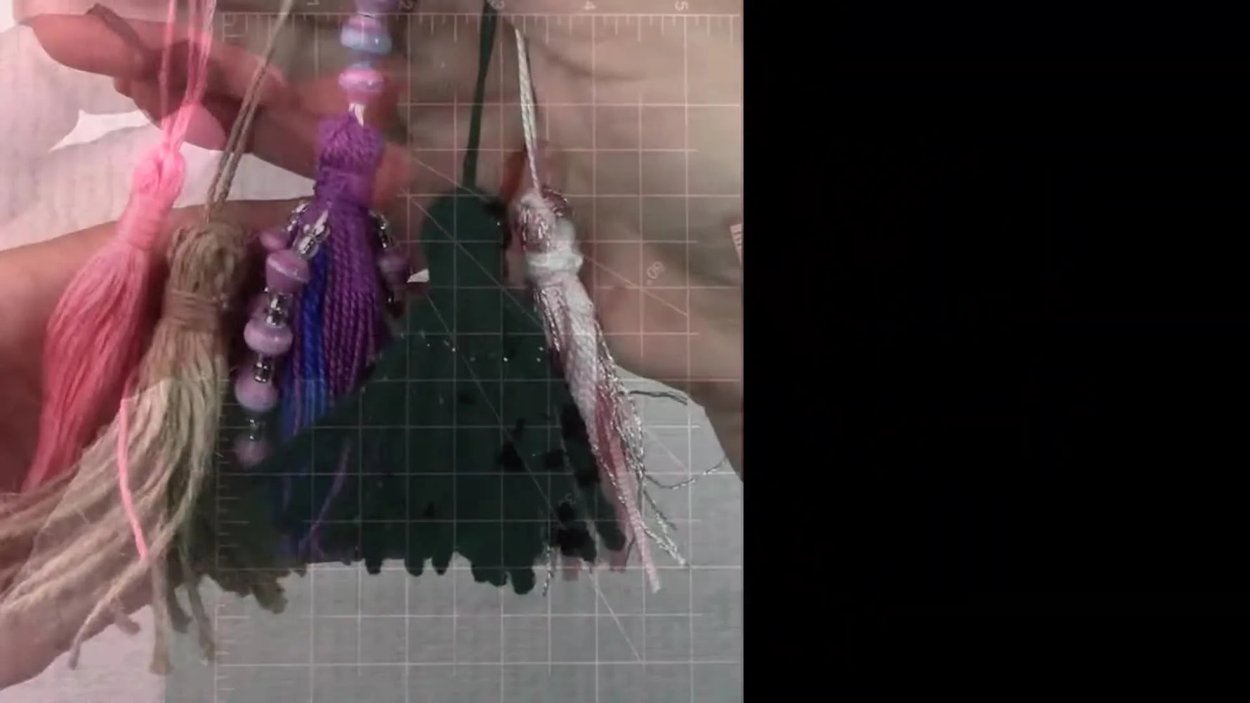 A hand holding a collection of five handmade tassels in different materials and colors: floss, twine, beaded floss, ribbon/metallic, and yarn.