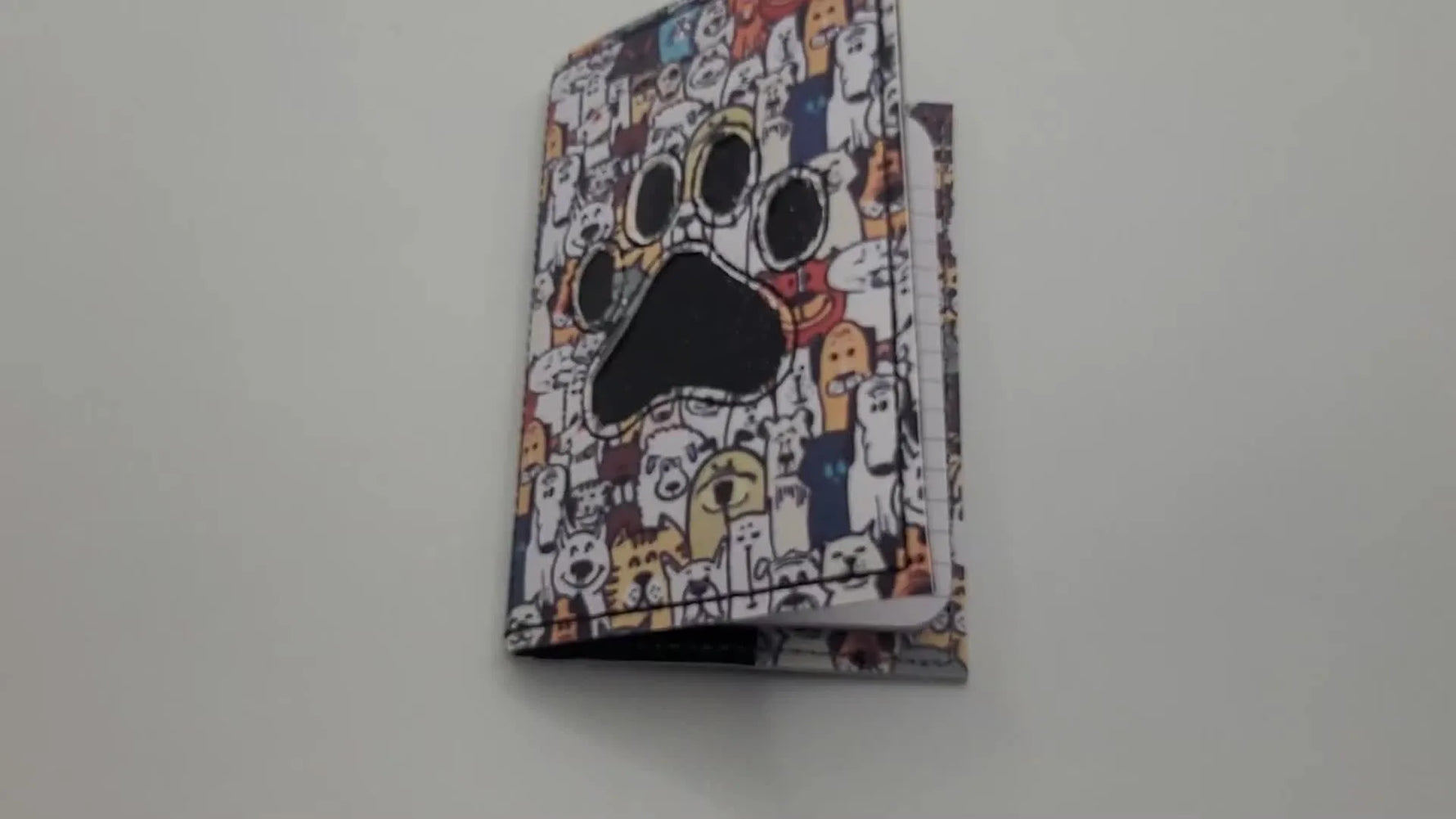 The finished 5x7 ITH notebook cover stands upright, showing a crisp reverse-appliqué paw print with a glitter underlayer and an elastic closure.